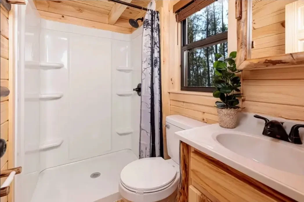 Cabin bathroom with a shower and vanity beside a woodland-facing window