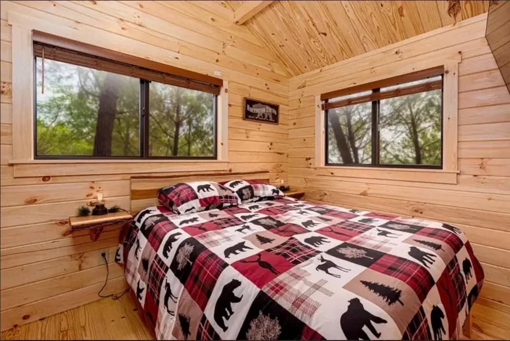 Cabin bedroom with a woodland-patterned quilt and windows overlooking the trees